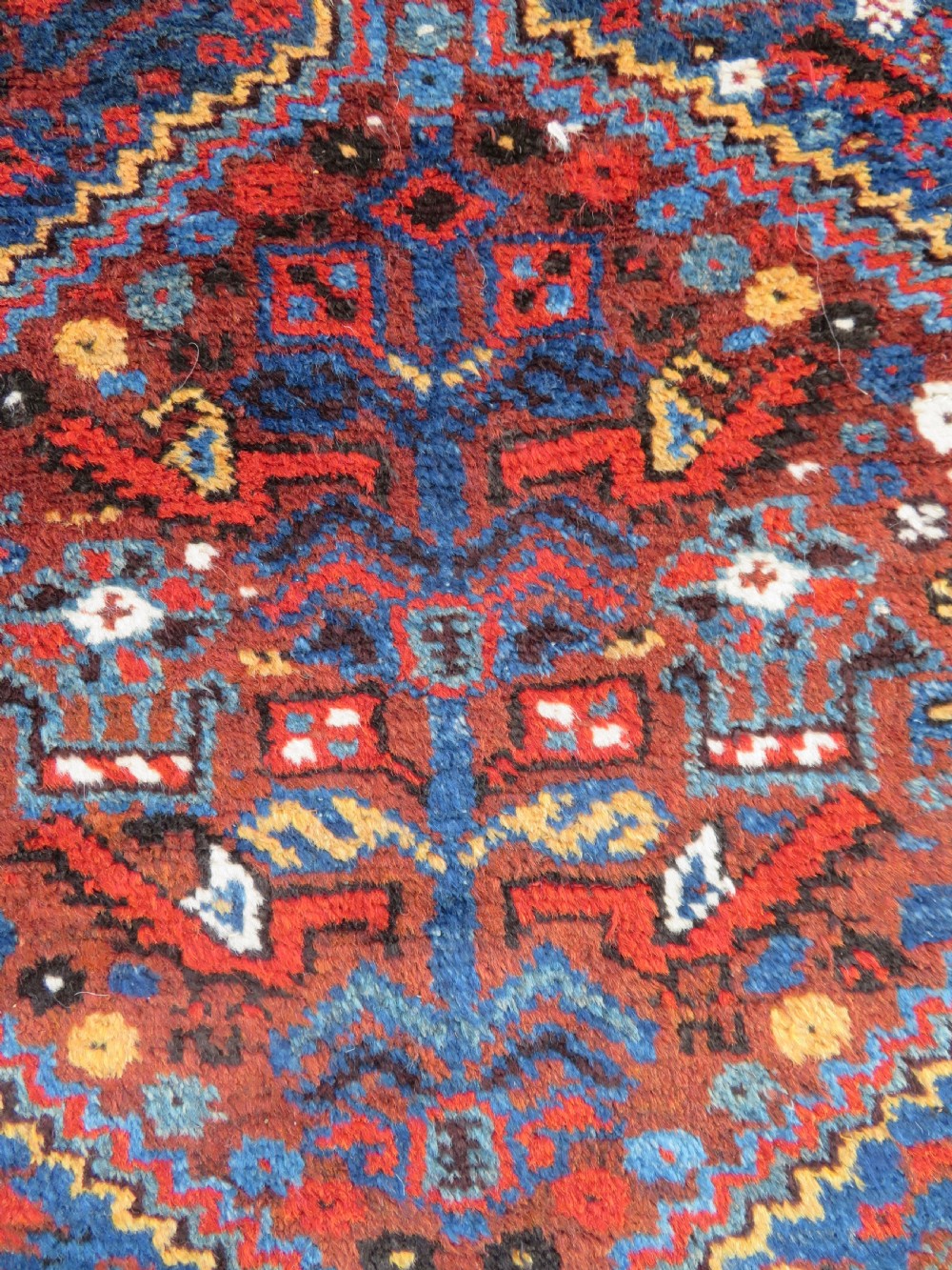 An antique Khamseh hand-knotted wool tribal rug featuring three central diamond medallions surrounded by small bird and geometric motifs in deep blue, terracotta red, and cream. View IV