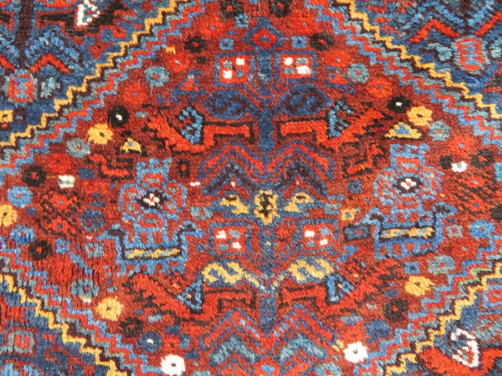 An antique Khamseh hand-knotted wool tribal rug featuring three central diamond medallions surrounded by small bird and geometric motifs in deep blue, terracotta red, and cream. View V