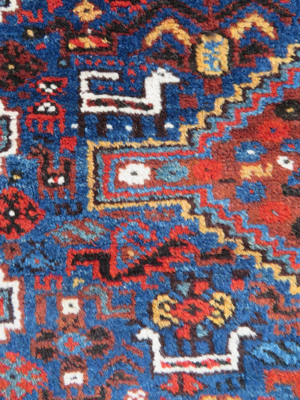 An antique Khamseh hand-knotted wool tribal rug featuring three central diamond medallions surrounded by small bird and geometric motifs in deep blue, terracotta red, and cream. View VI