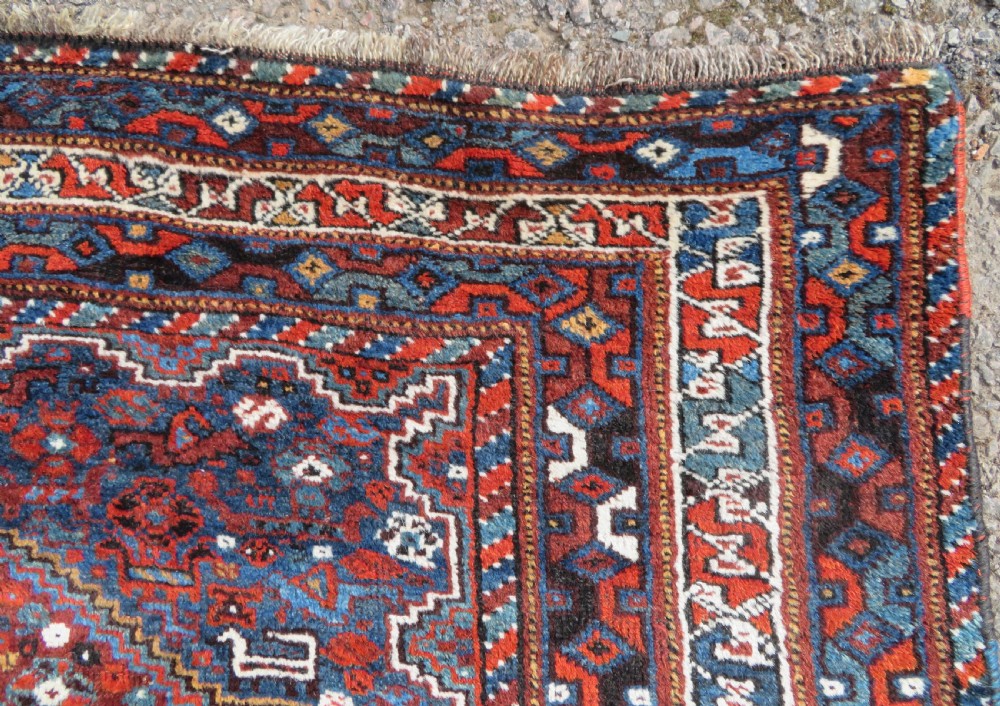 An antique Khamseh hand-knotted wool tribal rug featuring three central diamond medallions surrounded by small bird and geometric motifs in deep blue, terracotta red, and cream. View XII