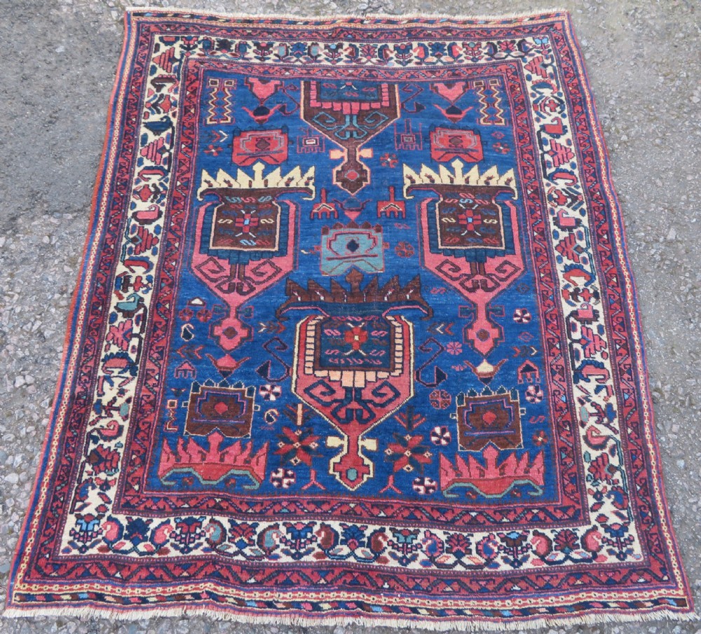 An antique hand-knotted Afshar wool rug featuring a vibrant indigo blue central field with stylized geometric medallions surrounded by detailed terracotta red and ivory borders.