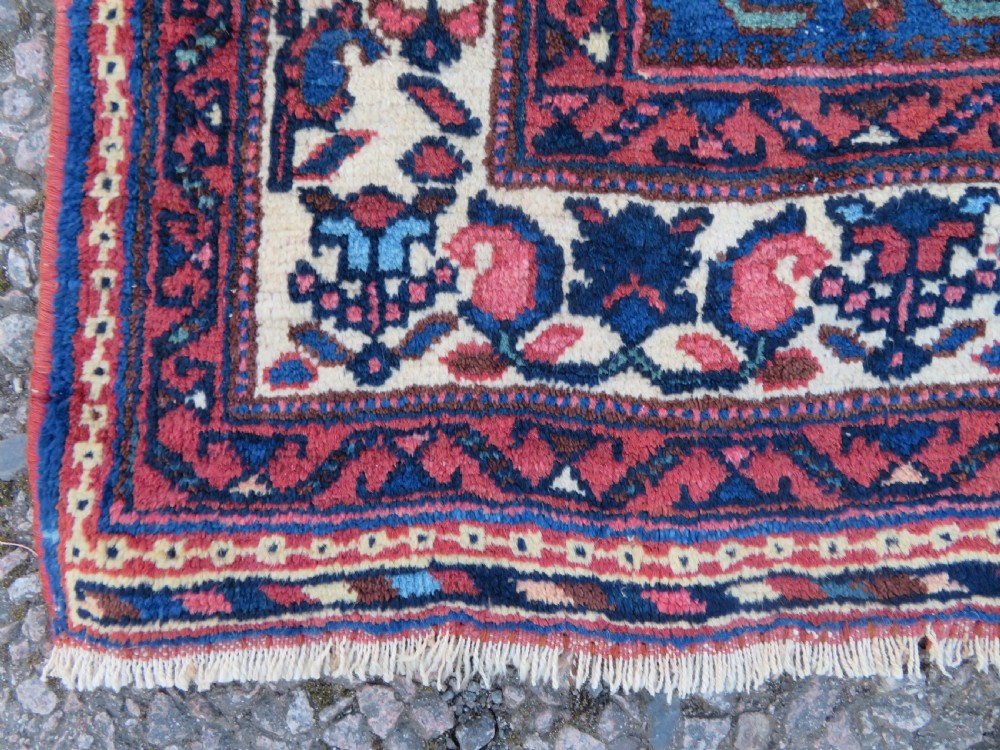 An antique hand-knotted Afshar wool rug featuring a vibrant indigo blue central field with stylized geometric medallions surrounded by detailed terracotta red and ivory borders. View V