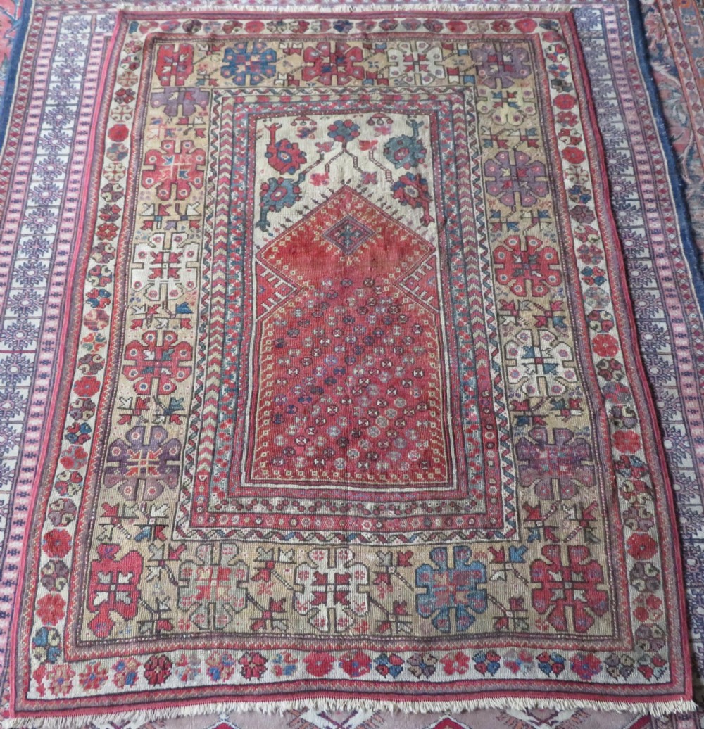 An antique hand-knotted Turkish Milas wool prayer rug featuring a central pointed arch motif in terracotta surrounded by broad geometric floral borders in cream, red, and blue shades.