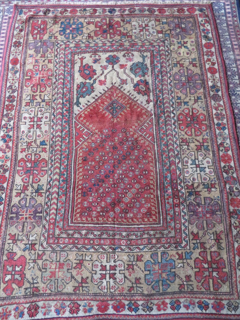 An antique hand-knotted Turkish Milas wool prayer rug featuring a central pointed arch motif in terracotta surrounded by broad geometric floral borders in cream, red, and blue shades. View II