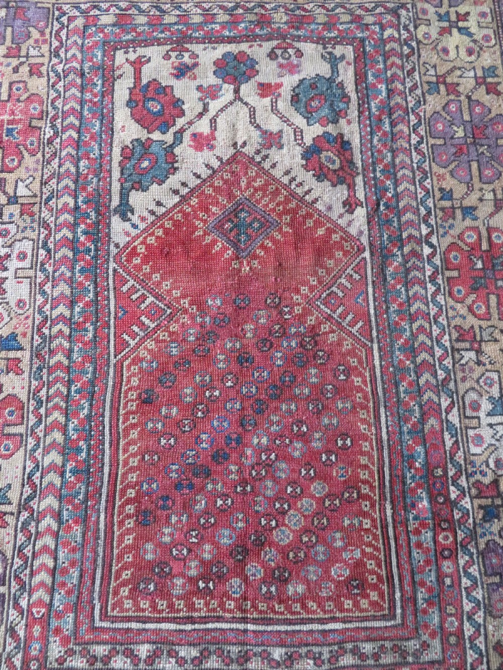 An antique hand-knotted Turkish Milas wool prayer rug featuring a central pointed arch motif in terracotta surrounded by broad geometric floral borders in cream, red, and blue shades. View III
