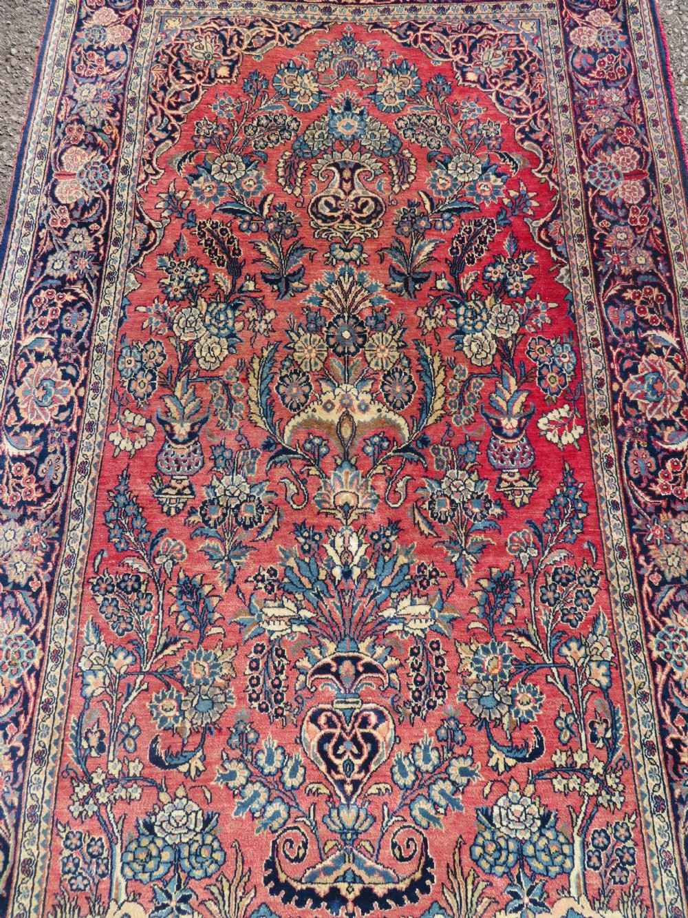 A rectangular hand-knotted Persian Kashan rug featuring a detailed crimson red field adorned with floral and vase motifs surrounded by a deep navy blue ornate border. View II