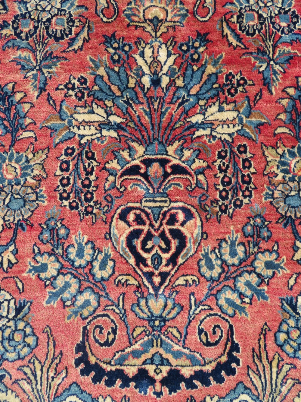 A rectangular hand-knotted Persian Kashan rug featuring a detailed crimson red field adorned with floral and vase motifs surrounded by a deep navy blue ornate border. View III