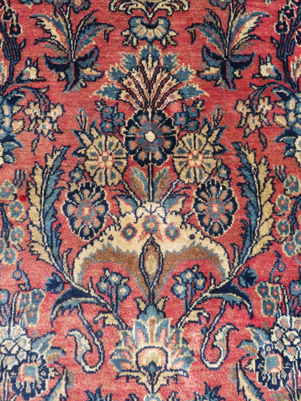 A rectangular hand-knotted Persian Kashan rug featuring a detailed crimson red field adorned with floral and vase motifs surrounded by a deep navy blue ornate border. View IV