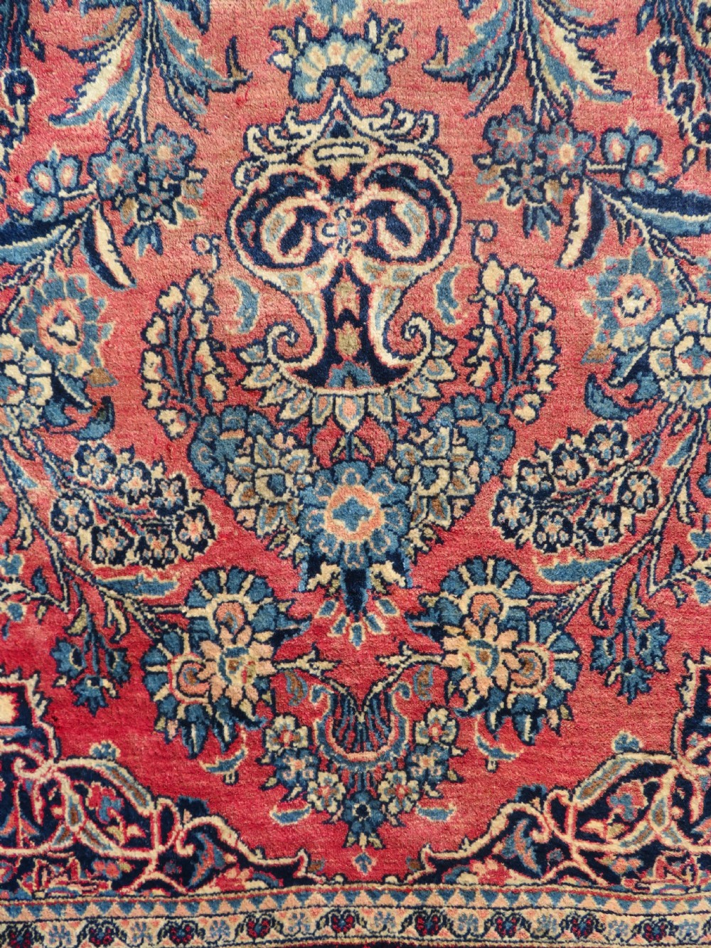 A rectangular hand-knotted Persian Kashan rug featuring a detailed crimson red field adorned with floral and vase motifs surrounded by a deep navy blue ornate border. View V