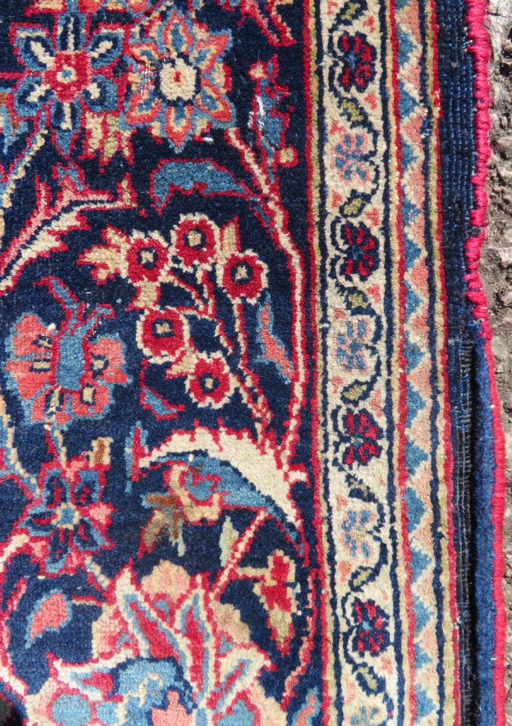 A rectangular hand-knotted Persian Kashan rug featuring a detailed crimson red field adorned with floral and vase motifs surrounded by a deep navy blue ornate border. View XI