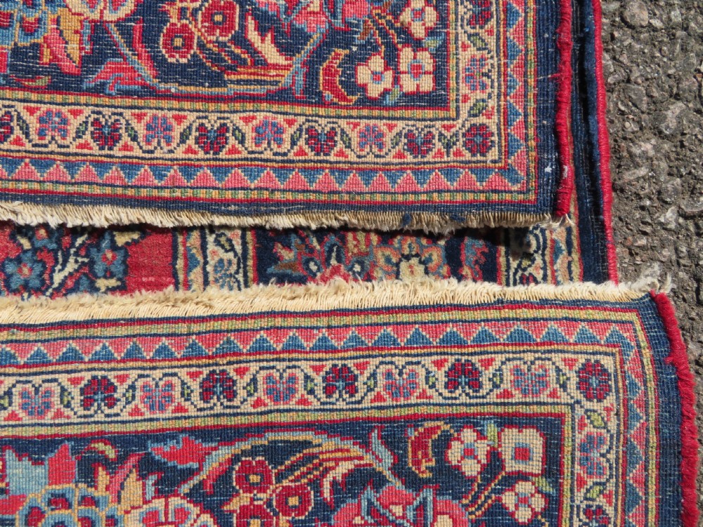 A rectangular hand-knotted Persian Kashan rug featuring a detailed crimson red field adorned with floral and vase motifs surrounded by a deep navy blue ornate border. View XIII