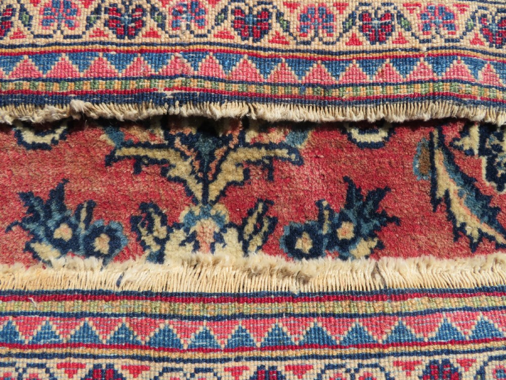 A rectangular hand-knotted Persian Kashan rug featuring a detailed crimson red field adorned with floral and vase motifs surrounded by a deep navy blue ornate border. View XIV