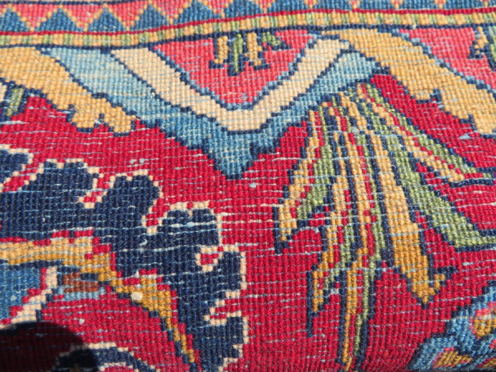 A rectangular hand-knotted Persian Kashan rug featuring a detailed crimson red field adorned with floral and vase motifs surrounded by a deep navy blue ornate border. View XV