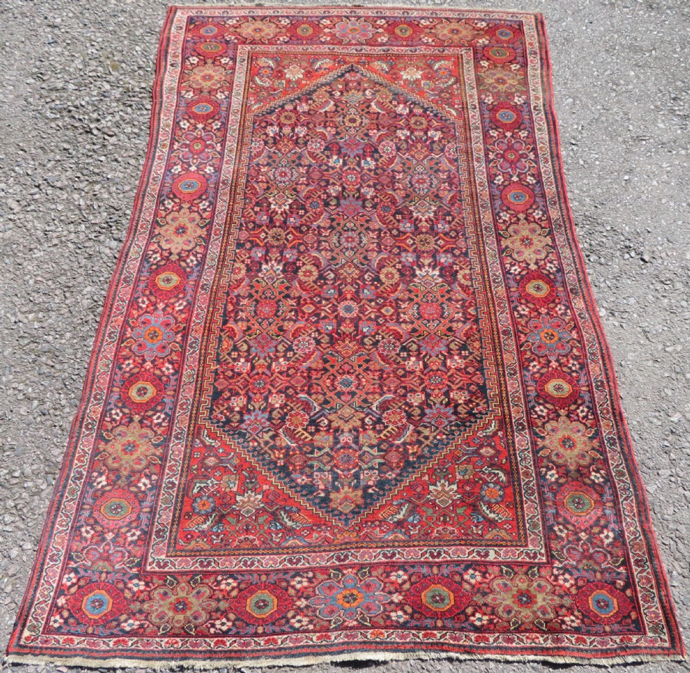 A hand-knotted antique Malayer rug featuring a central navy diamond medallion surrounded by elaborate geometric red and floral pattern borders.