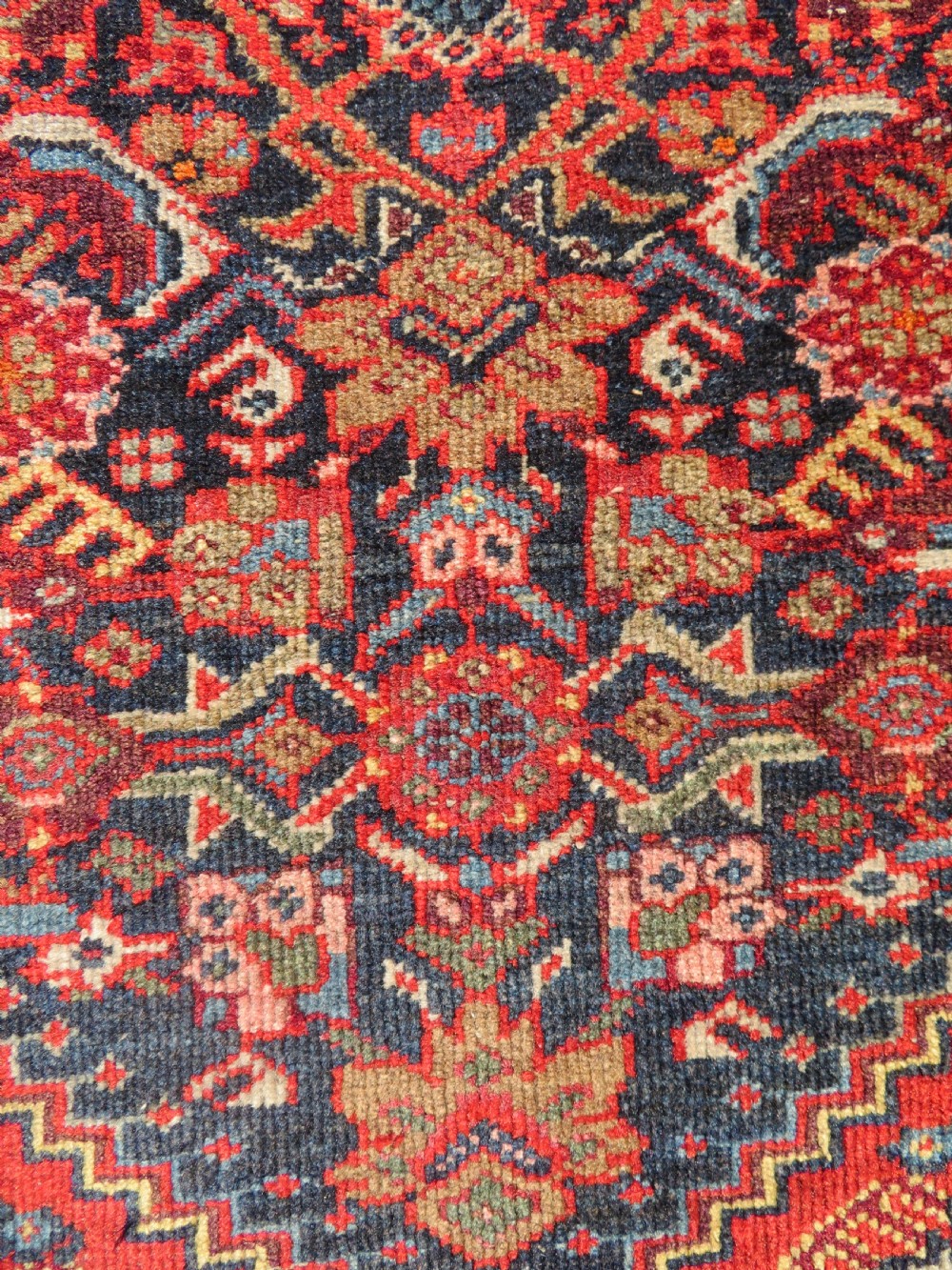 A hand-knotted antique Malayer rug featuring a central navy diamond medallion surrounded by elaborate geometric red and floral pattern borders. View III