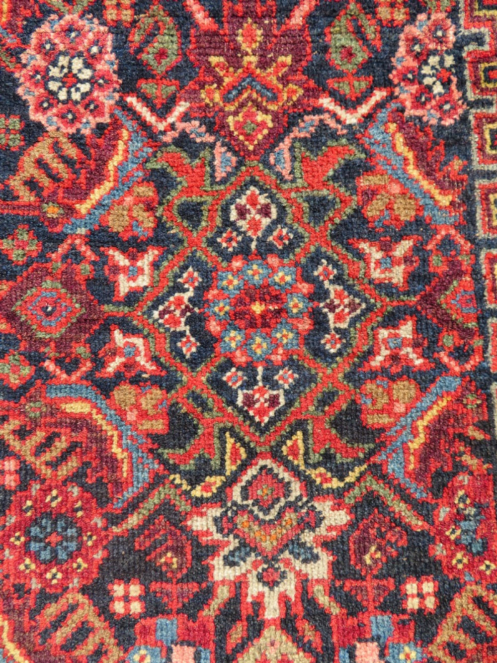 A hand-knotted antique Malayer rug featuring a central navy diamond medallion surrounded by elaborate geometric red and floral pattern borders. View VI