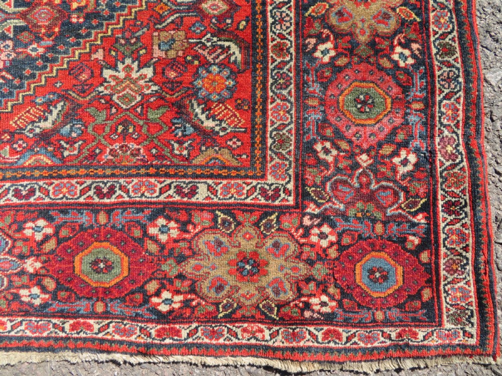 A hand-knotted antique Malayer rug featuring a central navy diamond medallion surrounded by elaborate geometric red and floral pattern borders. View IX