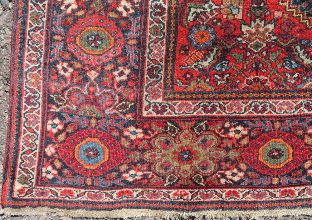 A hand-knotted antique Malayer rug featuring a central navy diamond medallion surrounded by elaborate geometric red and floral pattern borders. View X