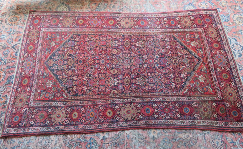 A hand-knotted antique Malayer rug featuring a central navy diamond medallion surrounded by elaborate geometric red and floral pattern borders. View XVII
