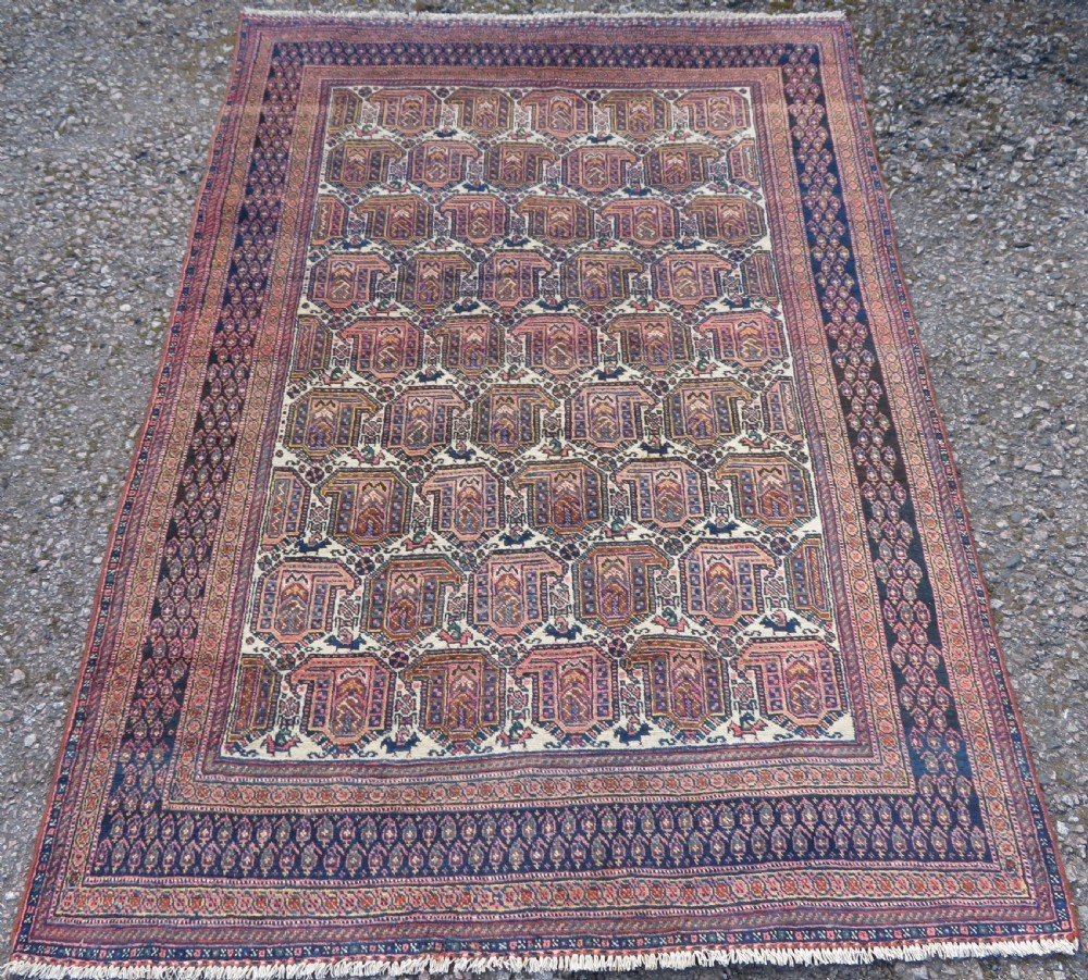 An antique hand-knotted Afshar wool rug featuring a repeating geometric motif on an ivory ground with dark blue and terracotta decorative borders.