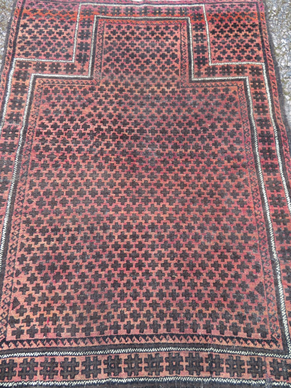 An antique Baluch prayer rug featuring a dark red and brown geometric grid pattern inside a defined mihrab arch with woven fringed ends. View II