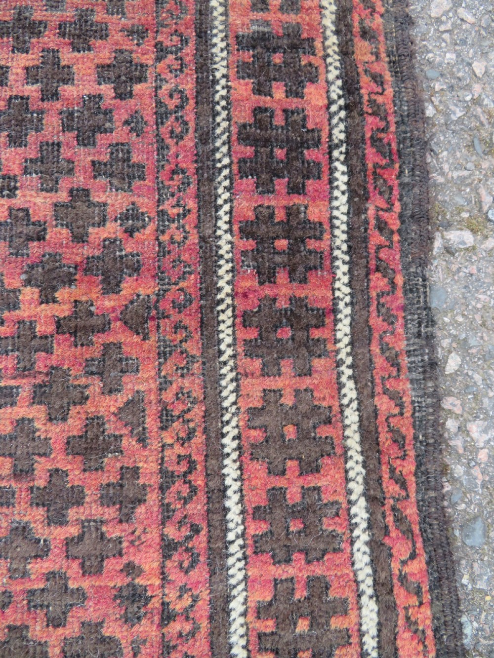 An antique Baluch prayer rug featuring a dark red and brown geometric grid pattern inside a defined mihrab arch with woven fringed ends. View IV