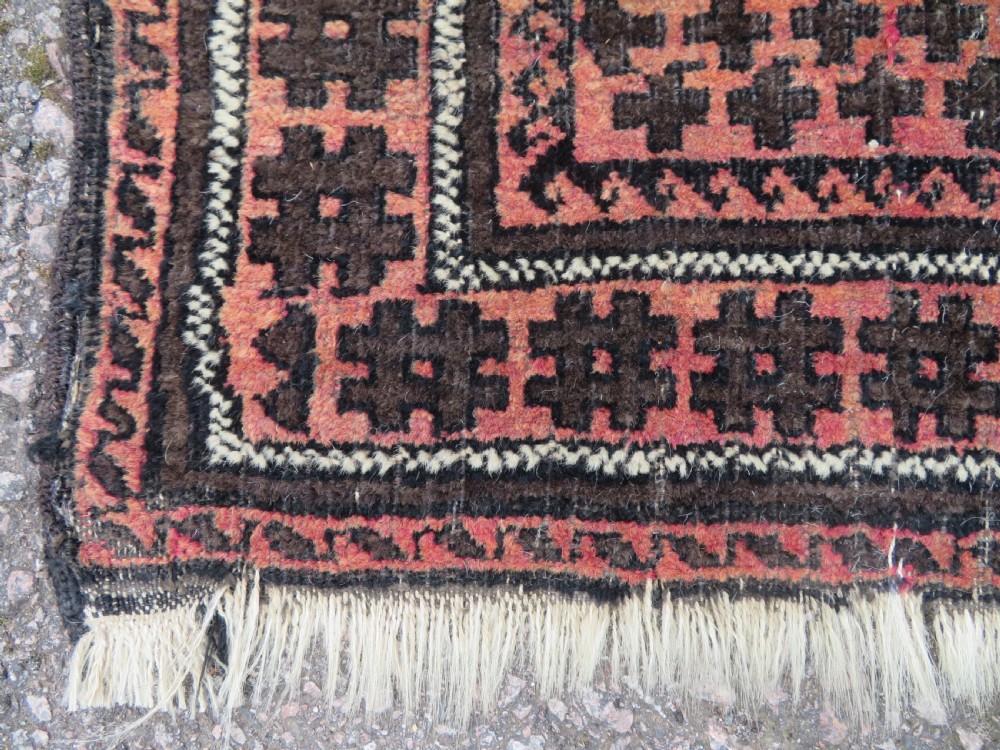An antique Baluch prayer rug featuring a dark red and brown geometric grid pattern inside a defined mihrab arch with woven fringed ends. View V