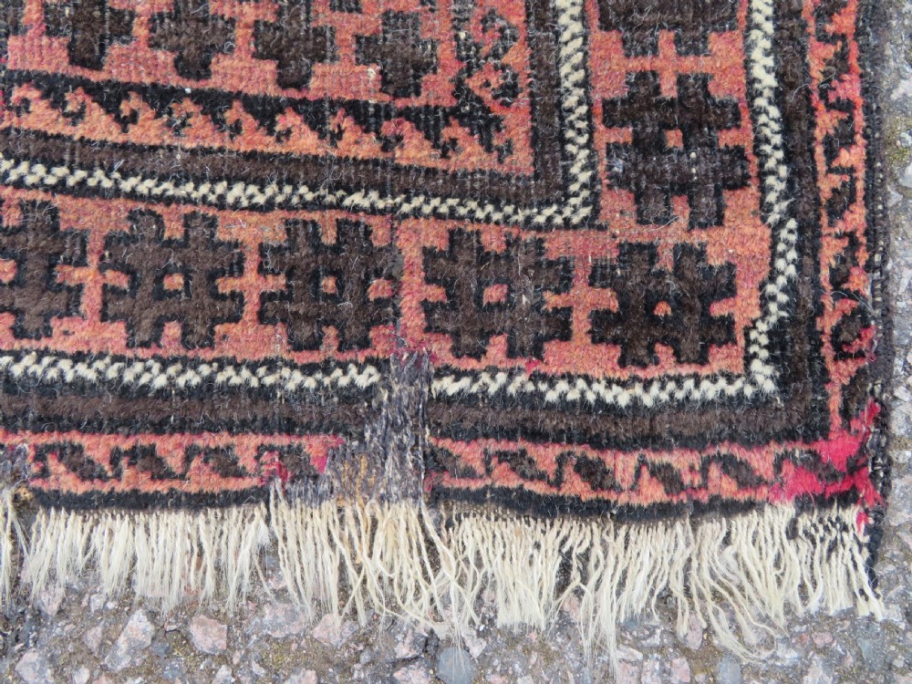 An antique Baluch prayer rug featuring a dark red and brown geometric grid pattern inside a defined mihrab arch with woven fringed ends. View VI
