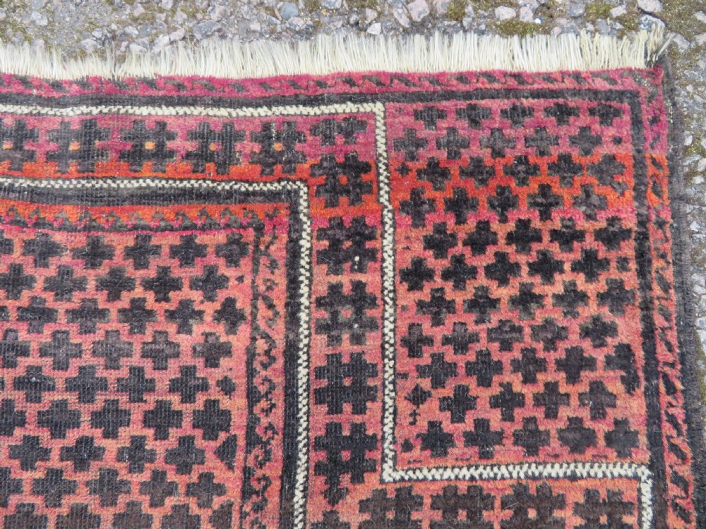 An antique Baluch prayer rug featuring a dark red and brown geometric grid pattern inside a defined mihrab arch with woven fringed ends. View VII