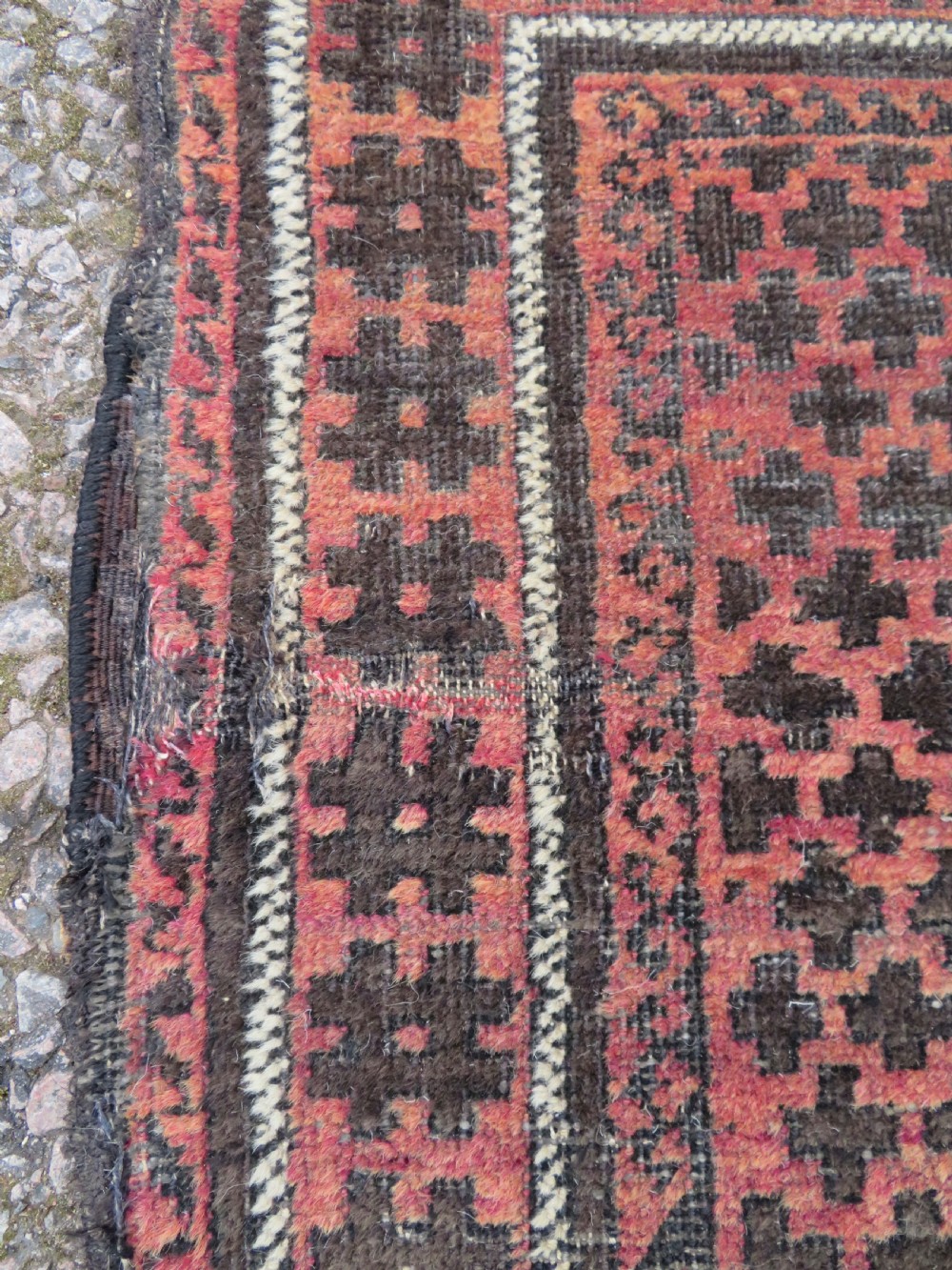 An antique Baluch prayer rug featuring a dark red and brown geometric grid pattern inside a defined mihrab arch with woven fringed ends. View IX