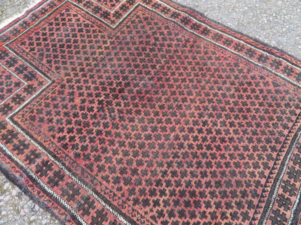 An antique Baluch prayer rug featuring a dark red and brown geometric grid pattern inside a defined mihrab arch with woven fringed ends. View X