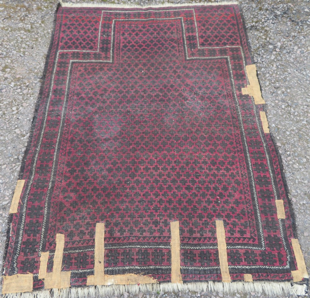 An antique Baluch prayer rug featuring a dark red and brown geometric grid pattern inside a defined mihrab arch with woven fringed ends. View XI