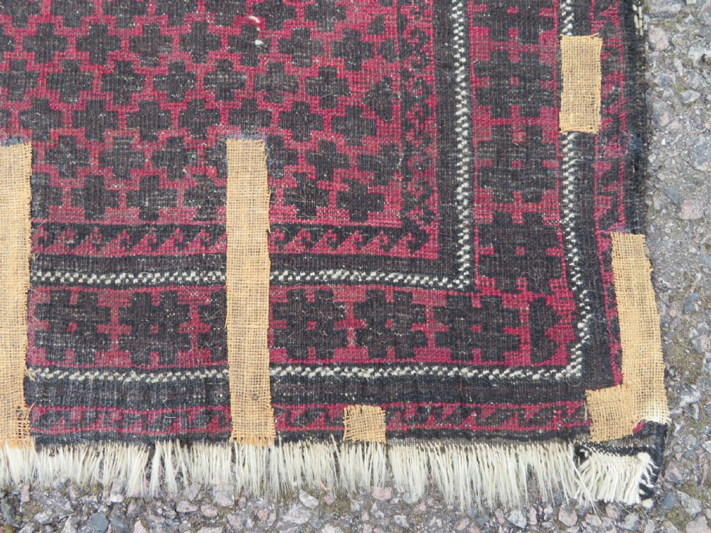 An antique Baluch prayer rug featuring a dark red and brown geometric grid pattern inside a defined mihrab arch with woven fringed ends. View XIII