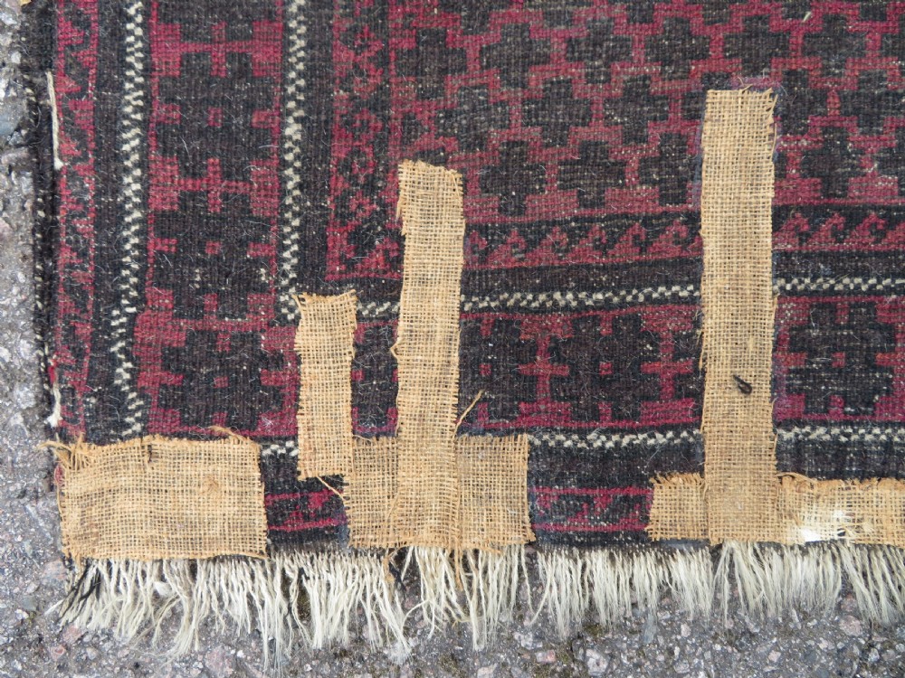 An antique Baluch prayer rug featuring a dark red and brown geometric grid pattern inside a defined mihrab arch with woven fringed ends. View XIV