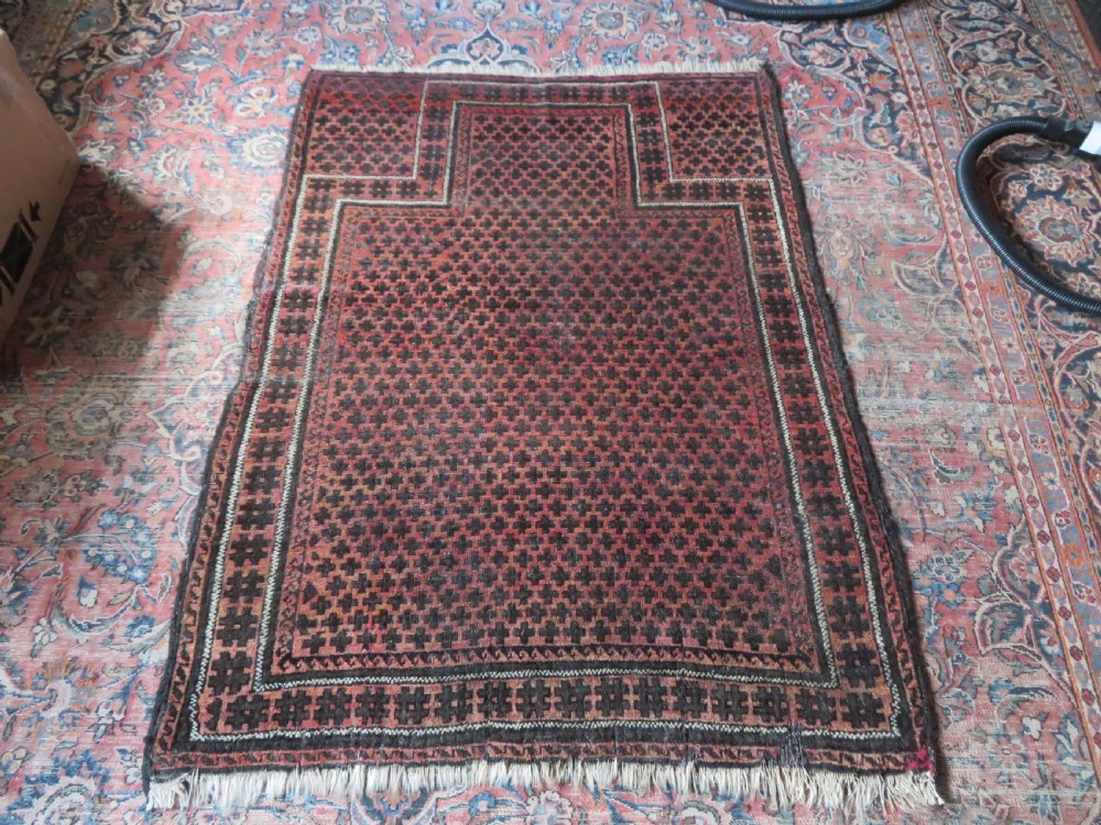 An antique Baluch prayer rug featuring a dark red and brown geometric grid pattern inside a defined mihrab arch with woven fringed ends. View XIX