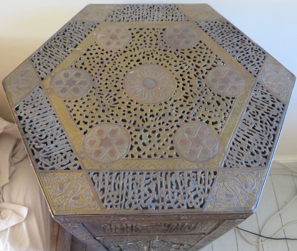 A tall hexagonal brass occasional table featuring intricate openwork latticework, Arabic calligraphic bands, copper and white-metal inlays, arched side openings, and turned feet. View II
