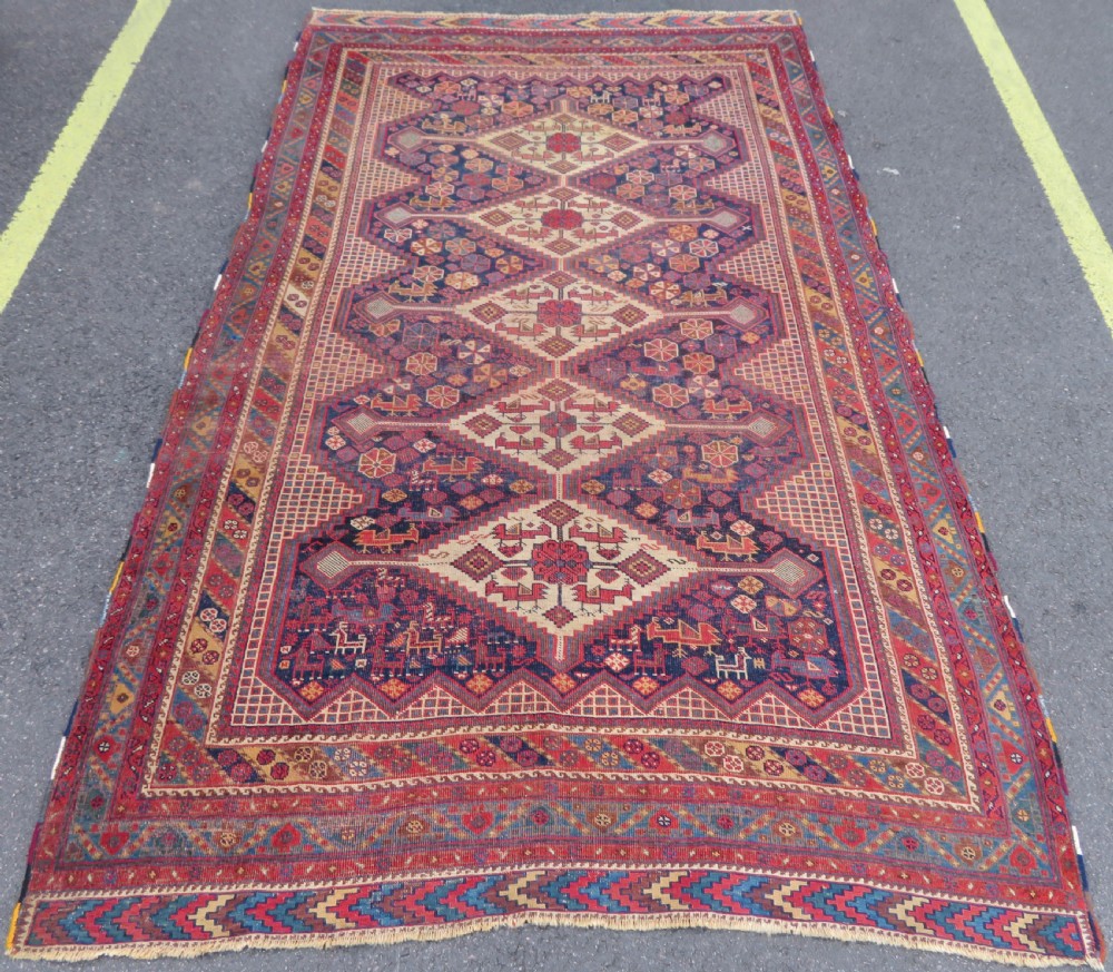 An antique Khamseh hand-knotted wool rug featuring five central diamond medallions on a dark navy and red field decorated with tribal bird motifs.