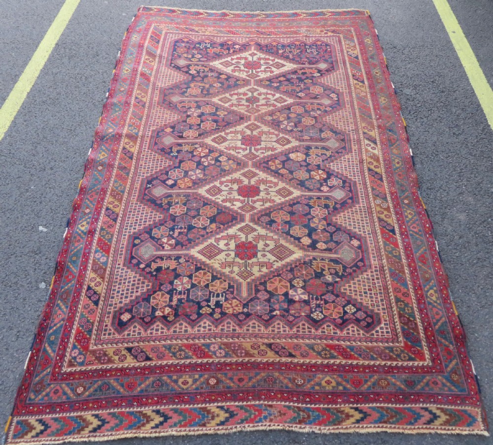 An antique Khamseh hand-knotted wool rug featuring five central diamond medallions on a dark navy and red field decorated with tribal bird motifs. View III