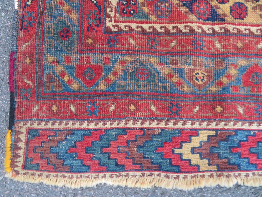 An antique Khamseh hand-knotted wool rug featuring five central diamond medallions on a dark navy and red field decorated with tribal bird motifs. View IV