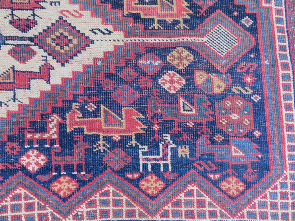 An antique Khamseh hand-knotted wool rug featuring five central diamond medallions on a dark navy and red field decorated with tribal bird motifs. View VI