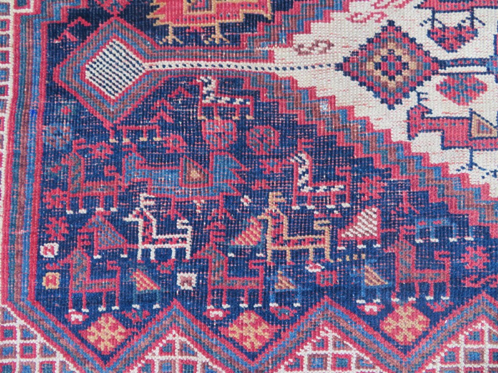 An antique Khamseh hand-knotted wool rug featuring five central diamond medallions on a dark navy and red field decorated with tribal bird motifs. View VII