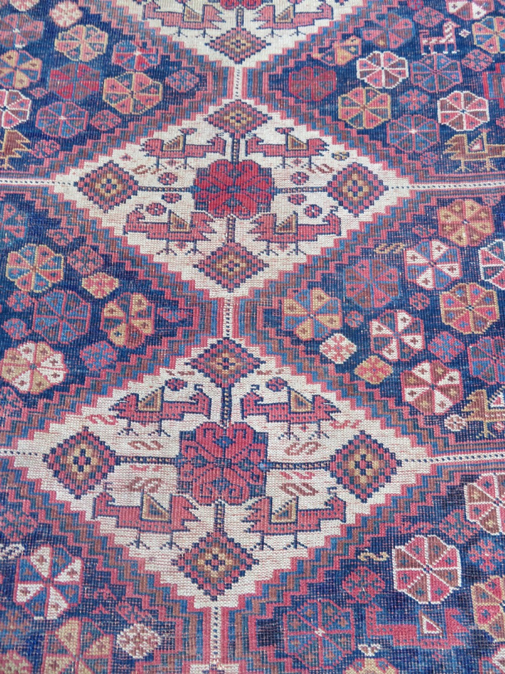 An antique Khamseh hand-knotted wool rug featuring five central diamond medallions on a dark navy and red field decorated with tribal bird motifs. View VIII