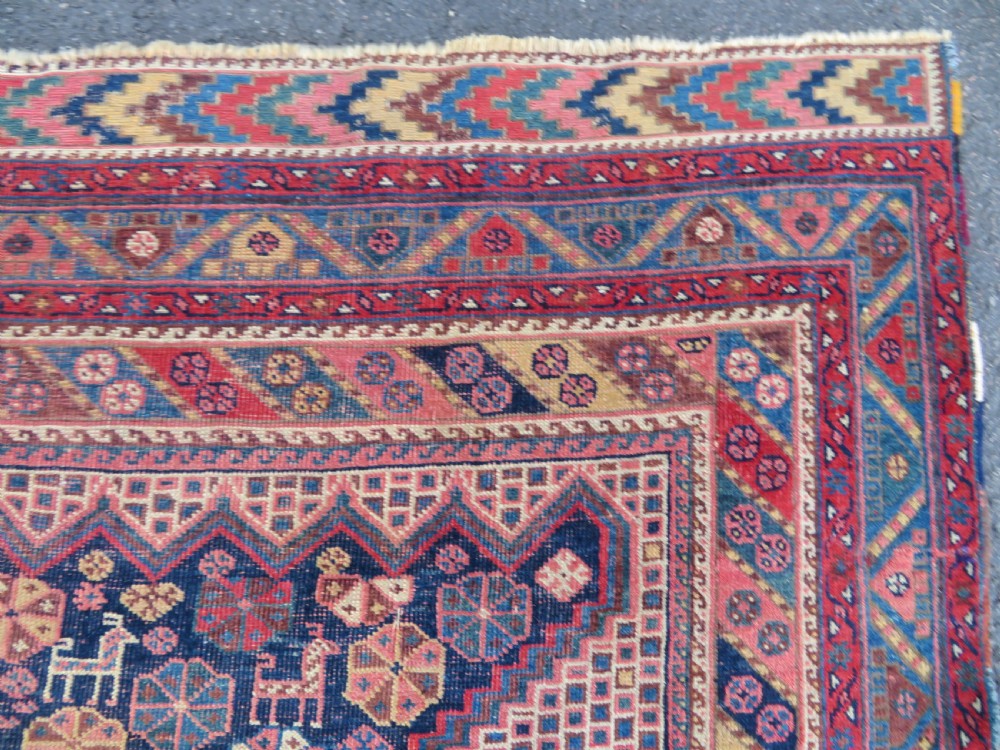 An antique Khamseh hand-knotted wool rug featuring five central diamond medallions on a dark navy and red field decorated with tribal bird motifs. View X
