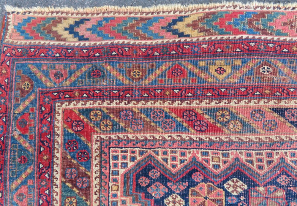 An antique Khamseh hand-knotted wool rug featuring five central diamond medallions on a dark navy and red field decorated with tribal bird motifs. View XI