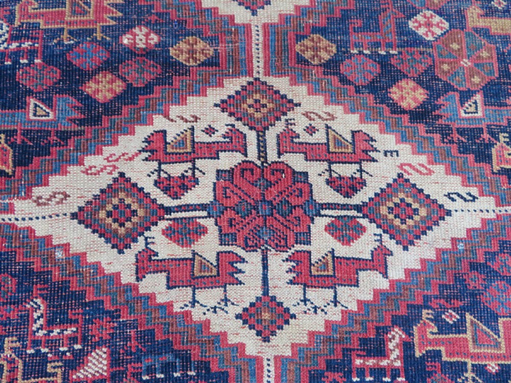 An antique Khamseh hand-knotted wool rug featuring five central diamond medallions on a dark navy and red field decorated with tribal bird motifs. View XVII