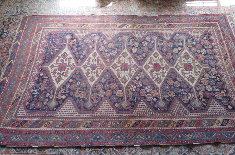 An antique Khamseh hand-knotted wool rug featuring five central diamond medallions on a dark navy and red field decorated with tribal bird motifs. View XXVI