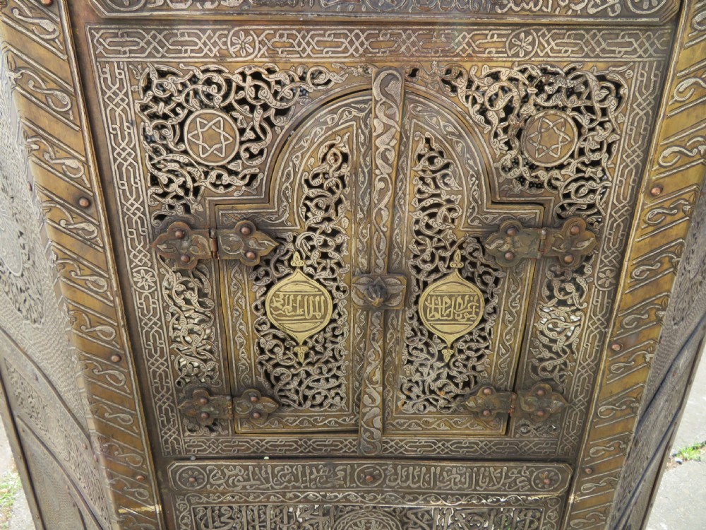 An octagonal brass and copper Cairoware Quran stand featuring Arabic calligraphy, pierced fretwork panels, silver inlay, and top dome finials crowned with crescent moons. View III
