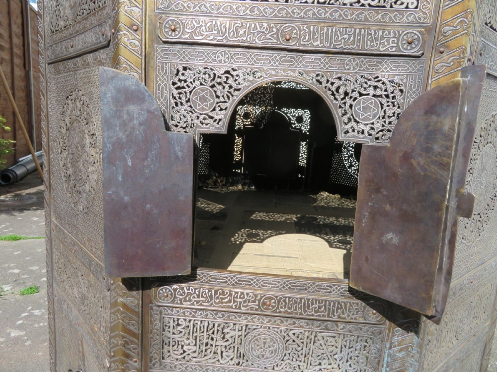 An octagonal brass and copper Cairoware Quran stand featuring Arabic calligraphy, pierced fretwork panels, silver inlay, and top dome finials crowned with crescent moons. View VII