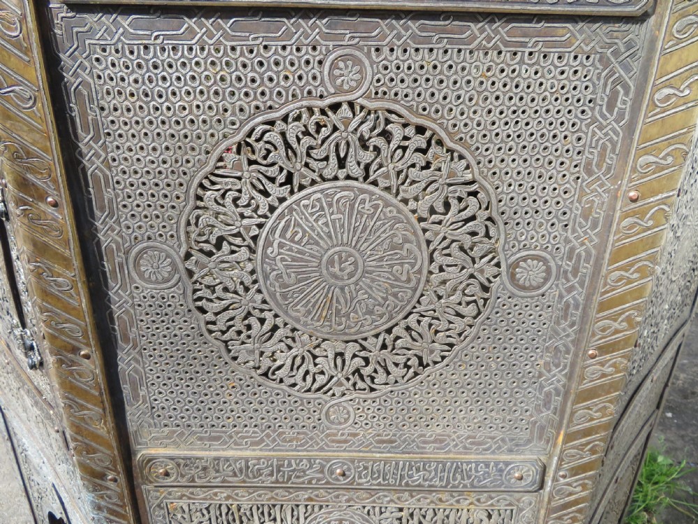 An octagonal brass and copper Cairoware Quran stand featuring Arabic calligraphy, pierced fretwork panels, silver inlay, and top dome finials crowned with crescent moons. View XI