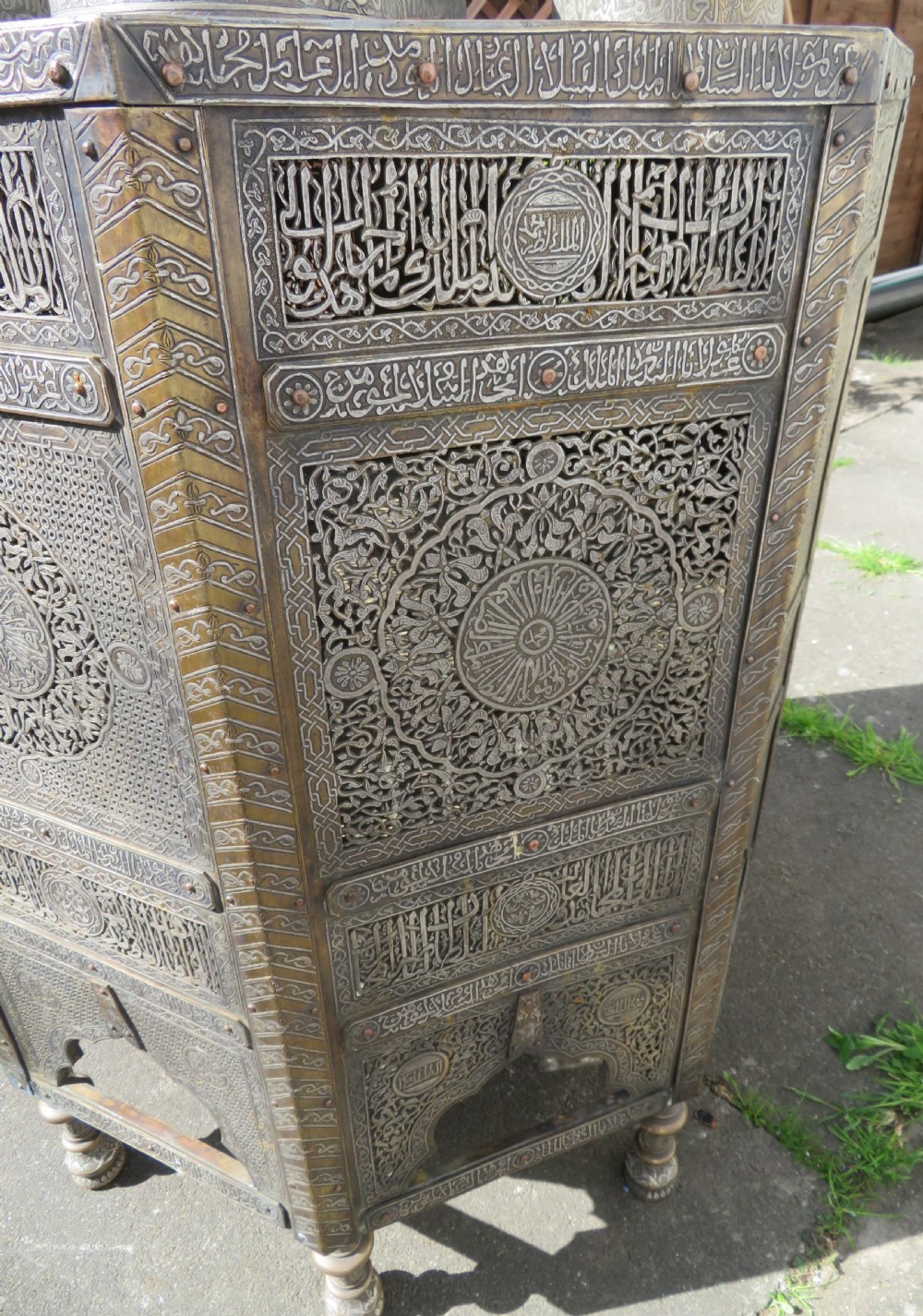 An octagonal brass and copper Cairoware Quran stand featuring Arabic calligraphy, pierced fretwork panels, silver inlay, and top dome finials crowned with crescent moons. View XIII